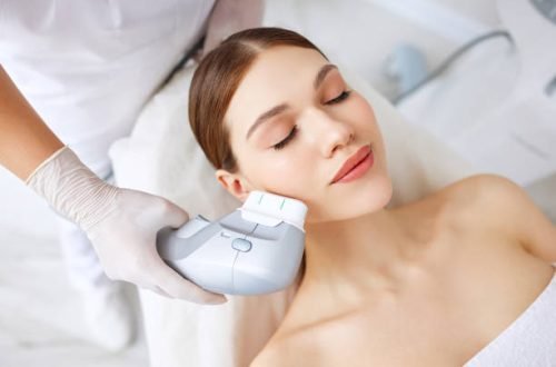 From above of relaxed young female client getting SMAS ultrasound face lifting massage with professional equipment in beauty center