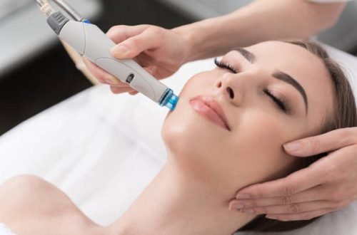 Close up portrait of young woman with closed eyes is lying on table while getting professional cosmetology procedure of hydro vacuum cleaner in beauty salon