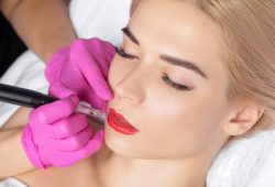 Permanent make-up for red Lips of beautiful blonde woman in beauty salon. Closeup beautician doing  tattooing Lips.